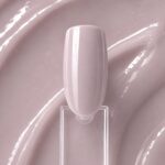 Polygel lichid nude Nudity N9 aplicat pe o mostră ovală pentru unghii, cu textura lucioasă a nuanței în fundal