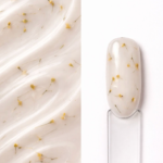 Builder gel Flora ButterMilk N9 aplicat pe o mostră ovală pentru unghii, cu inserții florale vizibile și textura gelului în fundal
