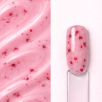 Builder gel Flora CherryMilk N9 aplicat pe o mostră ovală pentru unghii, cu inserții florale vizibile și textura gelului în fundal